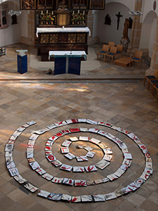 Innenraum einer gotischen Kirchen mit einer am Boden liegenden Spirale aus offenen bemalten Büchern
