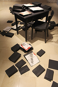 Installation Galerie im Halterhaus Leobersdorf, Tisch, Sessel, Bücher, Foto: Gerhard Kaiser Schwarzer Tisch und Sessel, auf dem Tisch und am Boden liegen zugeklappte Bücher und offene bezeichnete Blätter